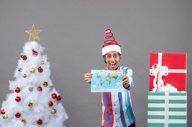 Hombre feliz de vista frontal con gorro de santa de resorte espiral mirando el mapa del mundo de alta tenencia