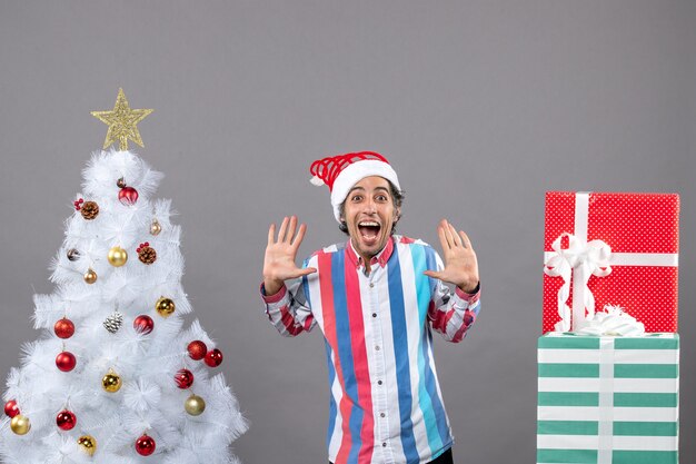 Hombre feliz de vista frontal de pie con las manos abiertas cerca del árbol de Navidad blanco