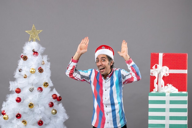 Hombre feliz de vista frontal poniendo sus manos cerca del árbol de Navidad blanco