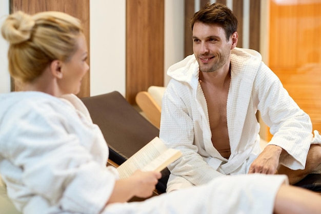 Hombre feliz vistiendo albornoz y hablando con su esposa mientras disfruta en el spa