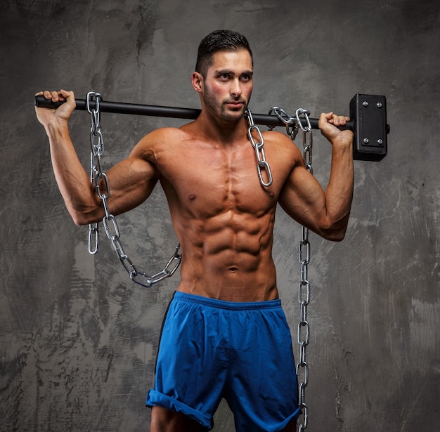 Foto gratuita hombre de fitness sin camisa muscular en pantalones cortos azules posando en estudio sobre fondo gris