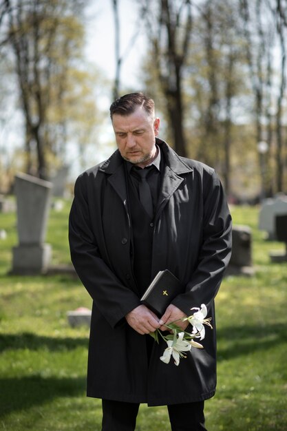 Hombre con flores y biblia en el cementerio.