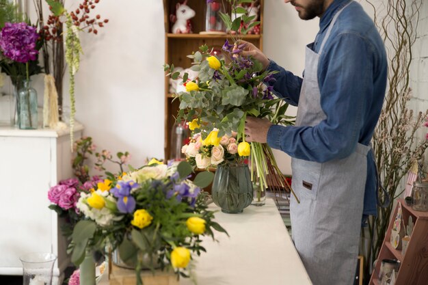 El hombre de la floristería en delantal hace un ramo en la floristería para un regalo festivo para una boda o aniversario