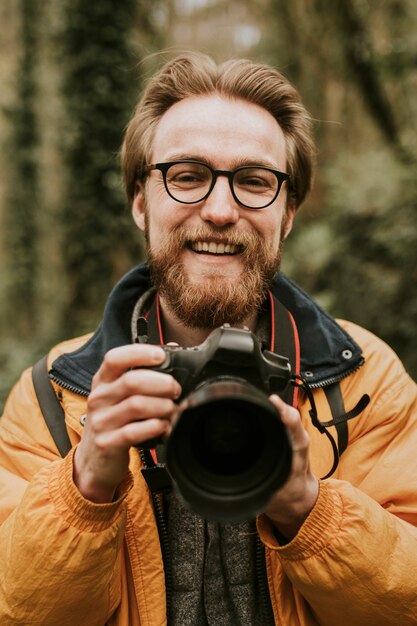 Hombre fotógrafo sonriendo mientras sostiene la cámara en el bosque