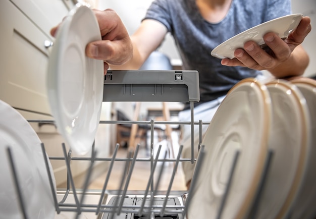 Foto gratuita un hombre frente a un lavavajillas abierto saca los platos limpios después de lavarlos.