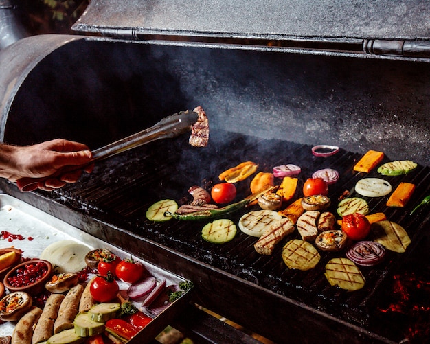 un hombre fríe verduras a la parrilla con salchichas