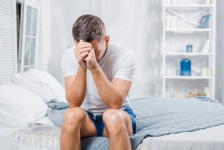 Foto gratuito hombre frustrado con dolor de cabeza sentado en la cama en su casa