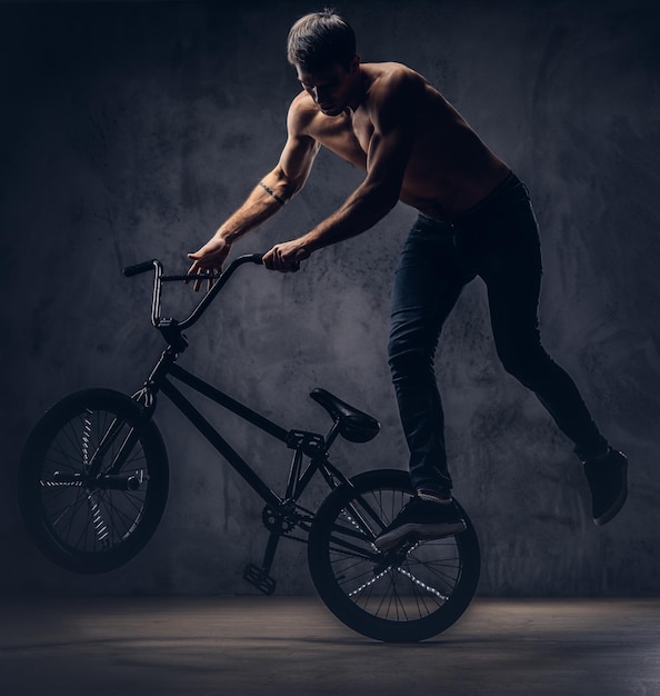 Foto gratuita hombre fuerte sin camisa, hace una figura acrobática con bmx en un estudio. aislado en un fondo oscuro.