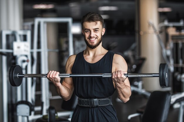 Hombre fuerte, culturista en ropa deportiva con pesas en un gimnasio, haciendo ejercicio con una barra