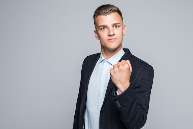 Hombre fuerte sonriente posando con teléfono portátil vestido con chaqueta oscura en estudio aislado en pared gris