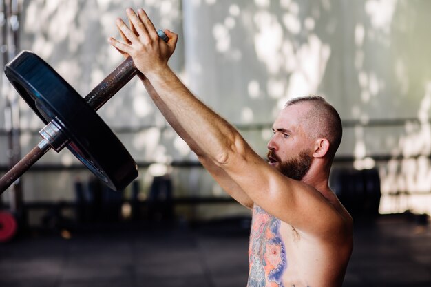 Hombre fuerte tatuado con barba en el gimnasio