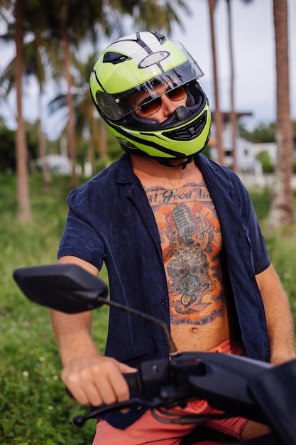 Foto gratuita hombre fuerte tatuado en el campo de la selva tropical con moto roja