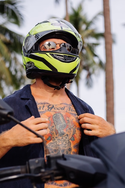 Hombre fuerte tatuado en el campo de la selva tropical con moto roja