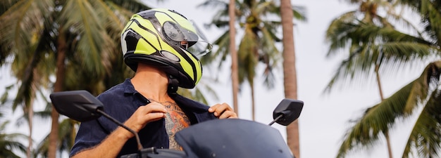 Hombre fuerte tatuado en el campo de la selva tropical con moto roja