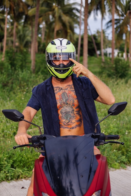 Hombre fuerte tatuado en el campo de la selva tropical con moto roja