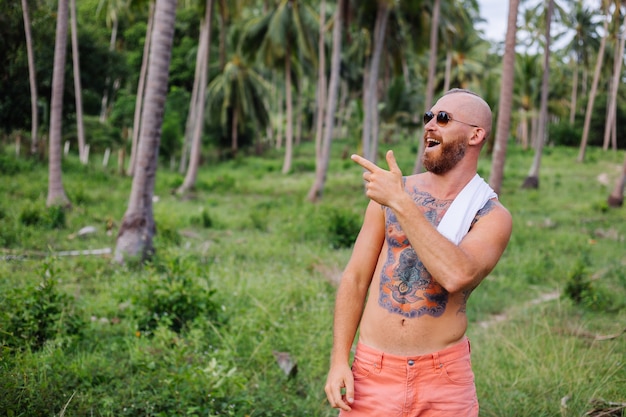 Hombre fuerte tatuado en el campo tropical de la selva sin camisa