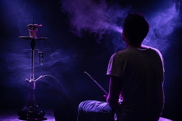 El hombre fumando la clásica shisha. Hermosos rayos de luz y humo de colores. El concepto de fumar pipa de agua.