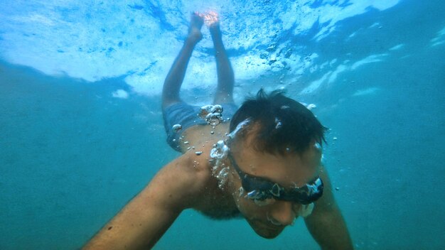 Hombre con gafas nadando bajo el agua azul y transparente del mar Mediterráneo. Sosteniendo la camara