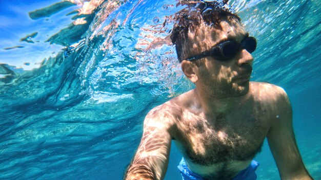 Hombre con gafas nadando bajo el agua azul y transparente del mar Mediterráneo. Sosteniendo la camara