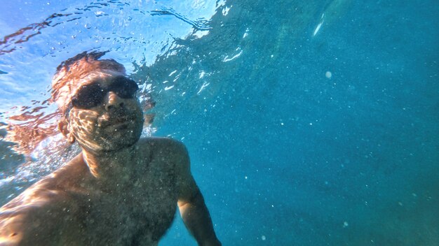 Hombre con gafas nadando bajo el agua azul y transparente del mar Mediterráneo. Sosteniendo la camara