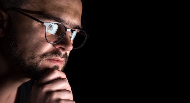 Un hombre con gafas en la oscuridad mira el espacio de copia de la pantalla de la computadora