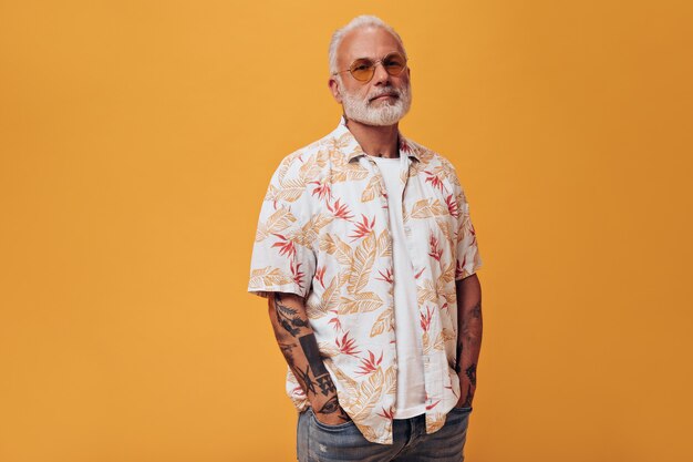 Hombre con gafas de sol naranjas y camisa mira al frente en la pared naranja