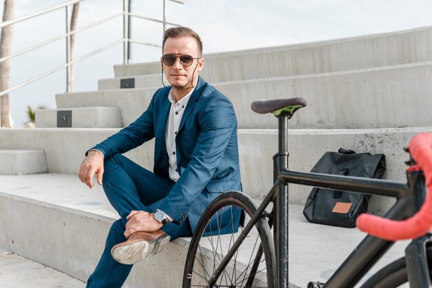 Hombre con gafas de sol sentado junto a su bicicleta al aire libre