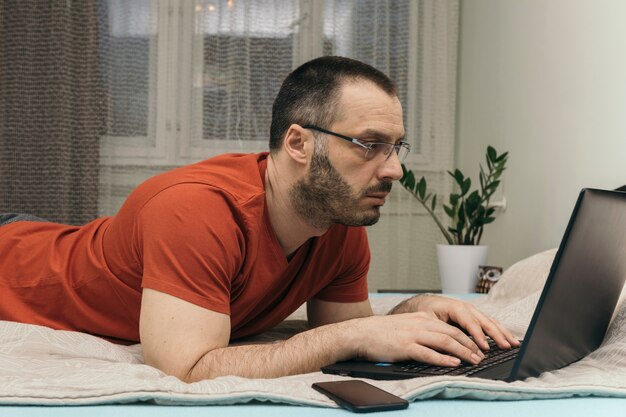 Hombre con gafas utilizando la computadora portátil en la cama