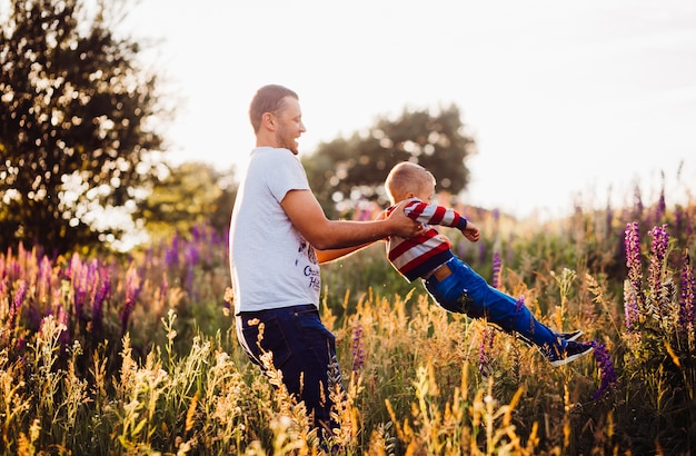 El hombre gira al pequeño hijo en el campo cubierto con luces de la tarde