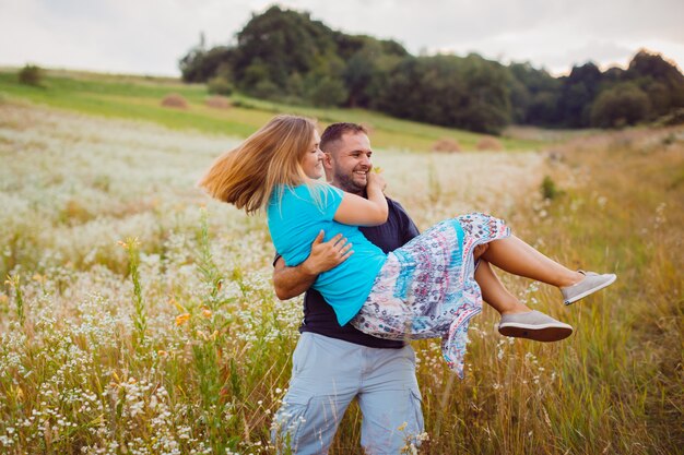 Hombre gira mujer rubia en los brazos de pie en el campo
