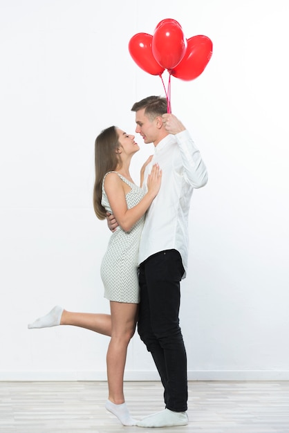 Hombre con globos de corazón abrazando a mujer