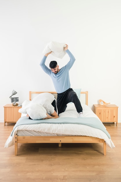 Hombre golpeando a su novio con almohada blanca en cama