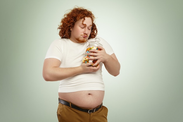 Foto gratuita hombre gordo voraz codicioso con pelo rizado rojo sosteniendo un tarro de dulces apretado