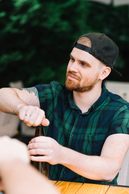 Hombre con gorra abriendo la botella de cerveza