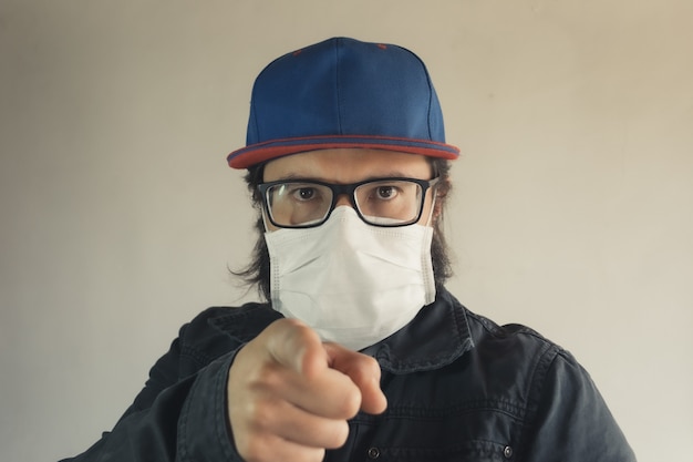 Foto gratuita hombre con gorra azul apuntando hacia ti con una mascarilla blanca para protegerte del polvo y el coronavirus