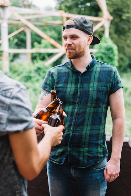 Foto gratuita hombre con gorra chocando las botellas de cerveza marrón con su amigo