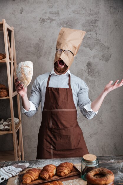 Hombre gritando panadero de pie con bolsa de papel en la cabeza