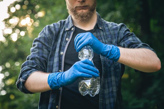 Un hombre con guantes y una botella de plástico en las manos limpia el bosque