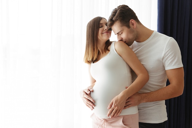 Hombre guapo abraza a su encantadora esposa embarazada en el interior en casa