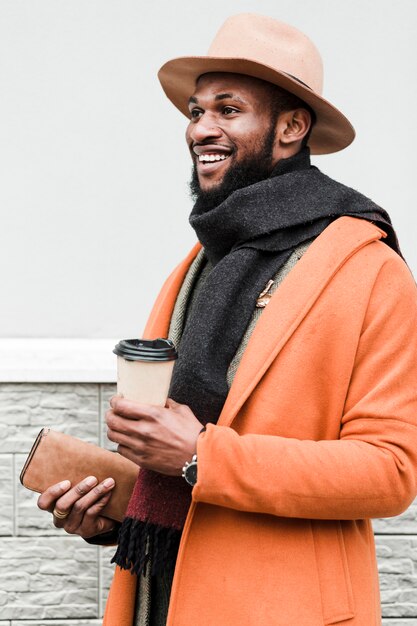 Hombre guapo con abrigo naranja sosteniendo su café y su billetera