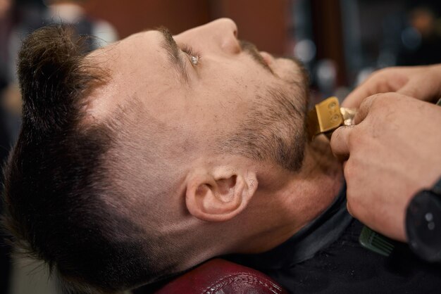 Hombre guapo acostado en el salón mientras el peluquero se corta la barba