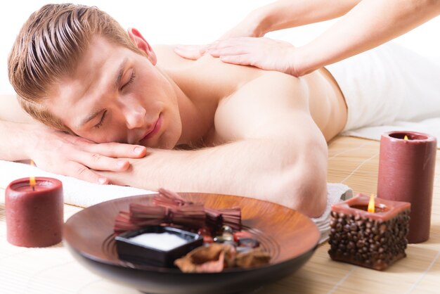 Hombre guapo acostado en un salón de spa disfrutando de un masaje de espalda de tejido profundo.