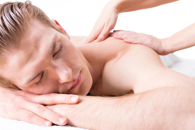 Hombre guapo acostado en un salón de spa disfrutando de un masaje de espalda de tejido profundo.