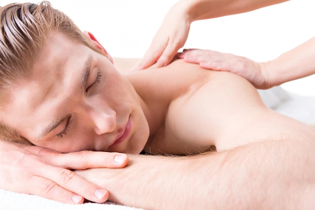 Hombre guapo acostado en un salón de spa disfrutando de un masaje de espalda de tejido profundo.