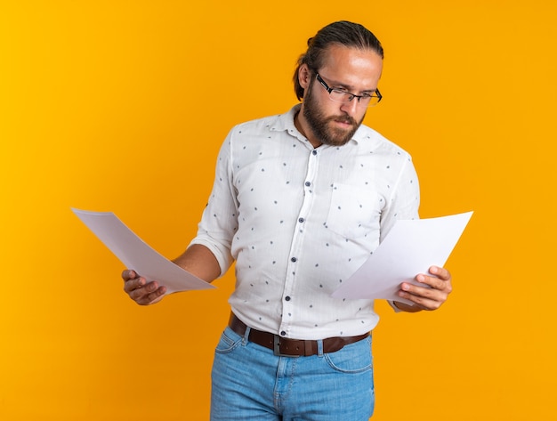 Foto gratuita hombre guapo adulto concentrado con gafas sosteniendo documentos mirando uno