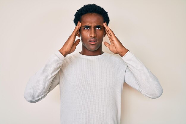 Hombre guapo africano con suéter de invierno casual que sufre de dolor de cabeza desesperado y estresado por el dolor y la migraña. manos en la cabeza.