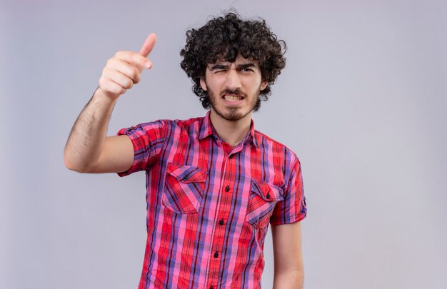 Un hombre guapo agresivo con el pelo rizado en camisa a cuadros apuntando a la cámara con el dedo índice