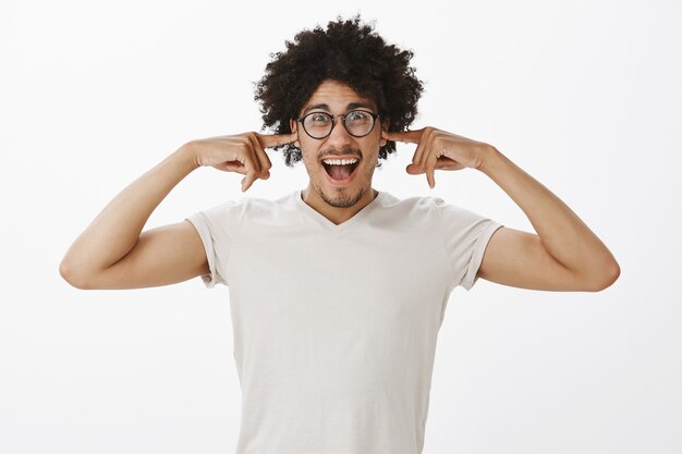 Hombre guapo alegre con gafas cerró los oídos y mirando emocionado, anticipando un fuerte golpe