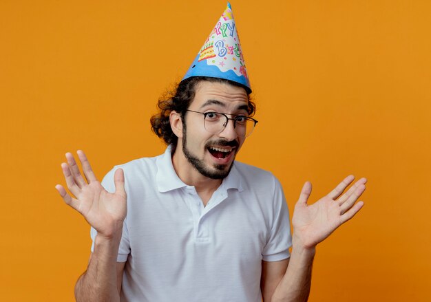 Foto gratuita hombre guapo alegre con gafas y gorro de cumpleaños extiende las manos aisladas sobre fondo naranja