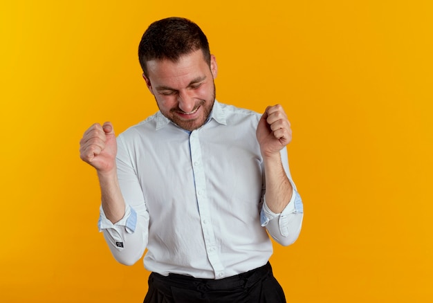 Hombre guapo alegre mantiene los puños con los ojos cerrados aislados en la pared naranja